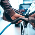 Human hand is holding Electric Car Charging connect to Electric car